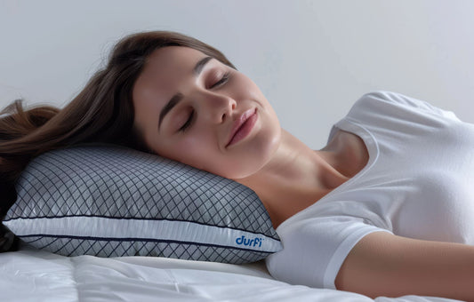 Woman sleeping comfortably on her side on a Durfi Dual Comfort Dr. Pillow with grey diamond-quilted cover and navy piping, shown on a white bed in a soft-lit bedroom