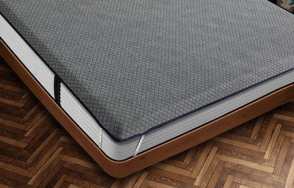 Close-up corner view of Durfi Essential Mattress Protector with grey diamond-quilted fabric and navy piping fitted snugly over a mattress on a warm brown wooden bed frame with herringbone parquet flooring