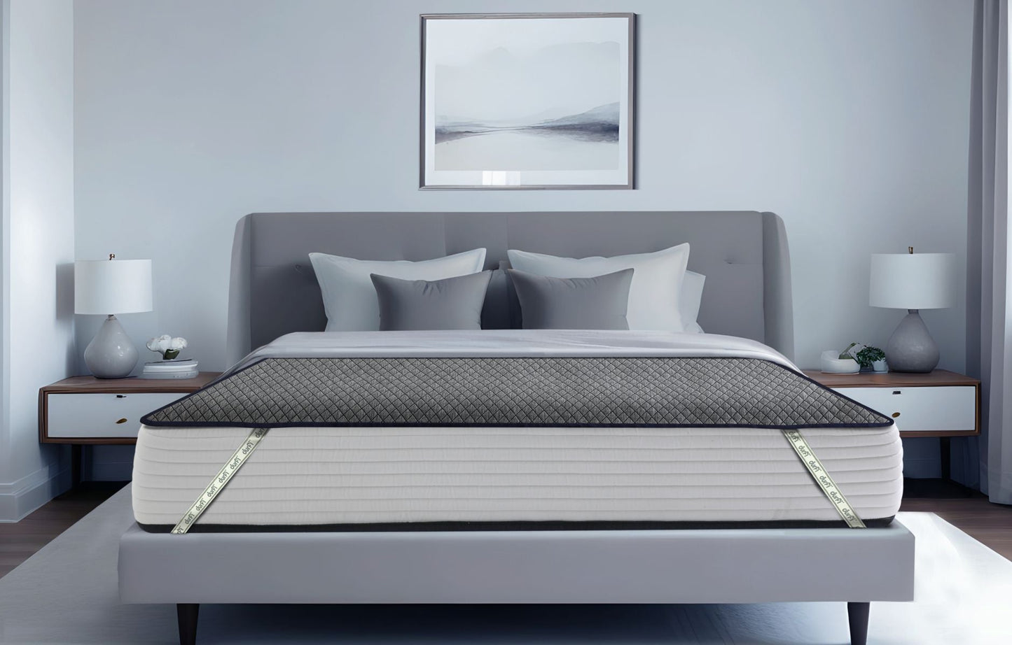 Durfi Essential Mattress Protector fitted over a mattress on a grey upholstered bed frame in a serene light grey bedroom with matching nightstands and table lamps
