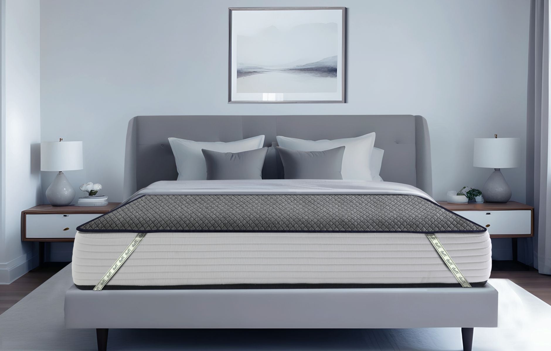 Durfi Essential Mattress Protector fitted over a mattress on a grey upholstered bed frame in a serene light grey bedroom with matching nightstands and table lamps