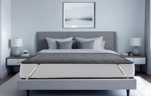 Durfi Essential Mattress Protector fitted over a mattress on a grey upholstered bed frame in a serene light grey bedroom with matching nightstands and table lamps