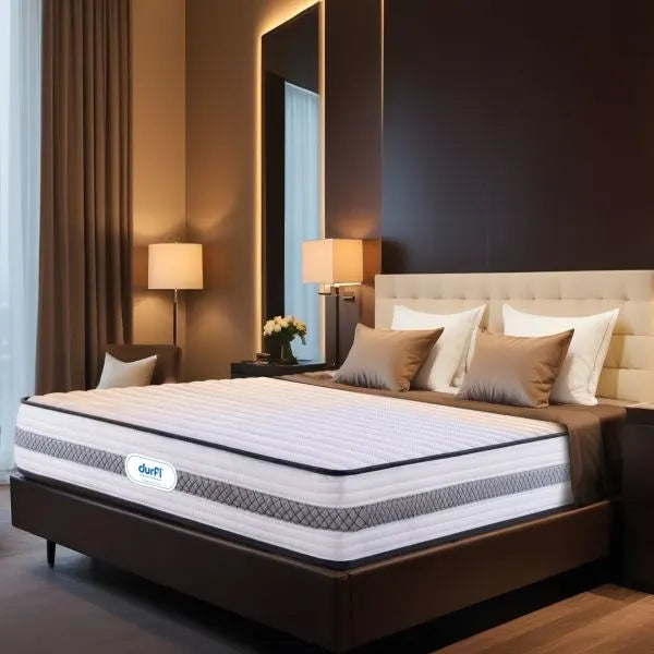 Durfi Hybrid Pocket Spring Mattress shown at an angle on a bed in an upscale hotel-style bedroom with a tall beige headboard, warm lighting, and decorative brown cushions