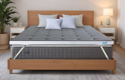 Durfi Soft Mattress Topper with grey tufted quilted surface placed over a mattress on a natural wood bed frame in a bright Scandinavian-style bedroom with indoor plants and white nightstands